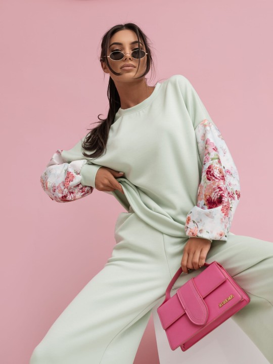 Zdjęcie przedstawia komplet damski dresowy w kolorze miętowym. Komplet składa się z bluzy i spodni. Bluza bez kaptura wkłada przez głowę z bufiastymi rękawami z efektownym kwiatowym wzorem. Spodnie z długimi i szerokimi nogawkami.